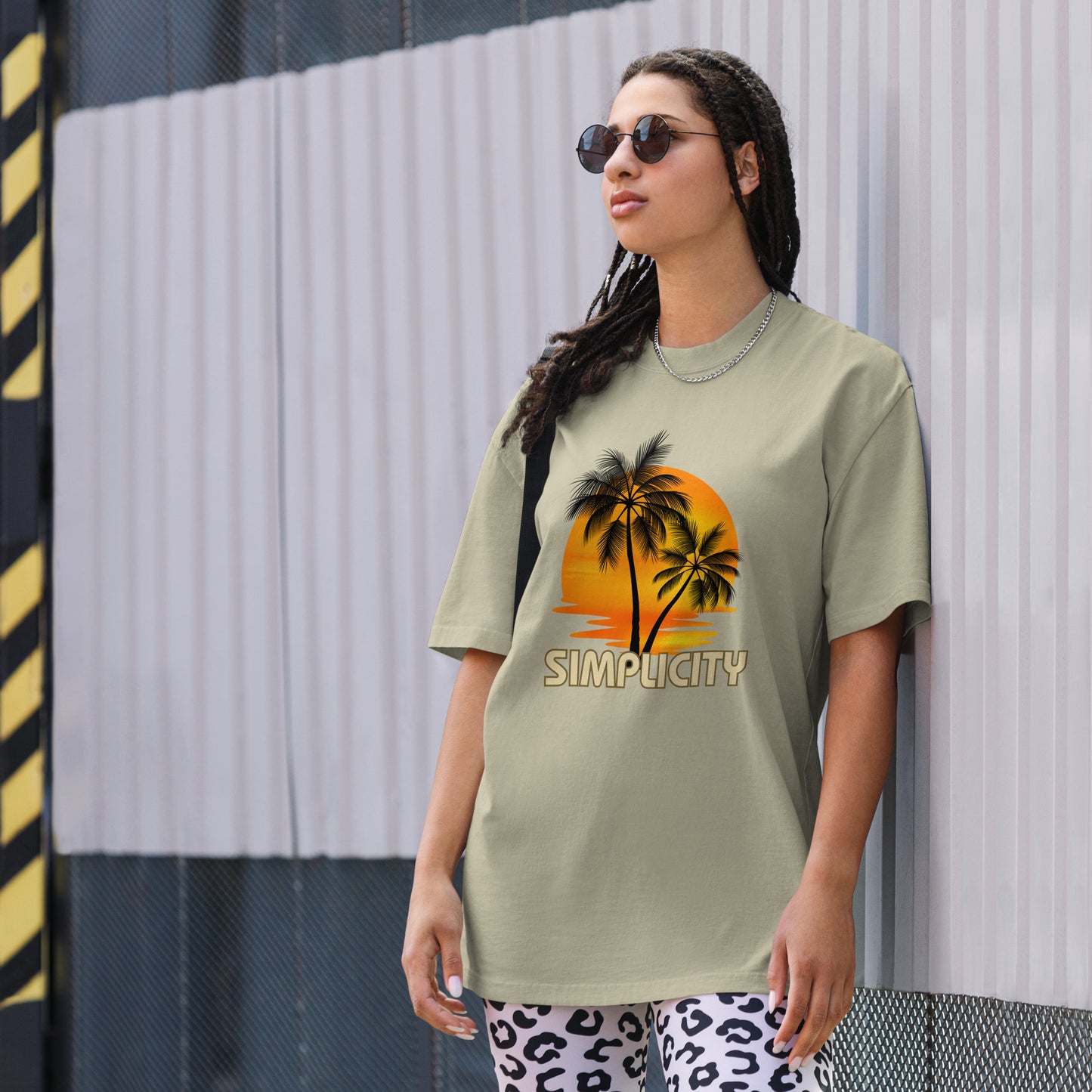 A woman in a Women's Sunset Simplicity faded eucalyptus Oversized Tee with a minimalist palm design in soft earth tones, exuding calm and trendy vibes.