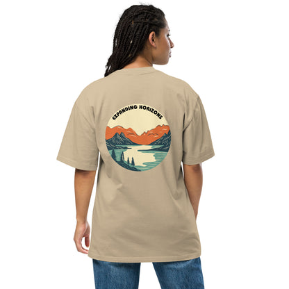 Woman wearing a faded khaki 'Expanding Horizons' Oversized Tee from Be You Out Loud, showcasing a scenic mountain and lake graphic in warm hues, signifying adventure and tranquility.