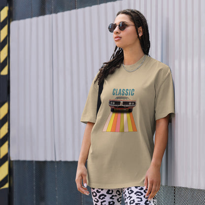 Cool and casual, a woman models a faded khaki 'CLASSIC' graphic tee featuring a vintage car cruising down a retro striped road, and paired with relaxed blue jeans and chic sunglasses.