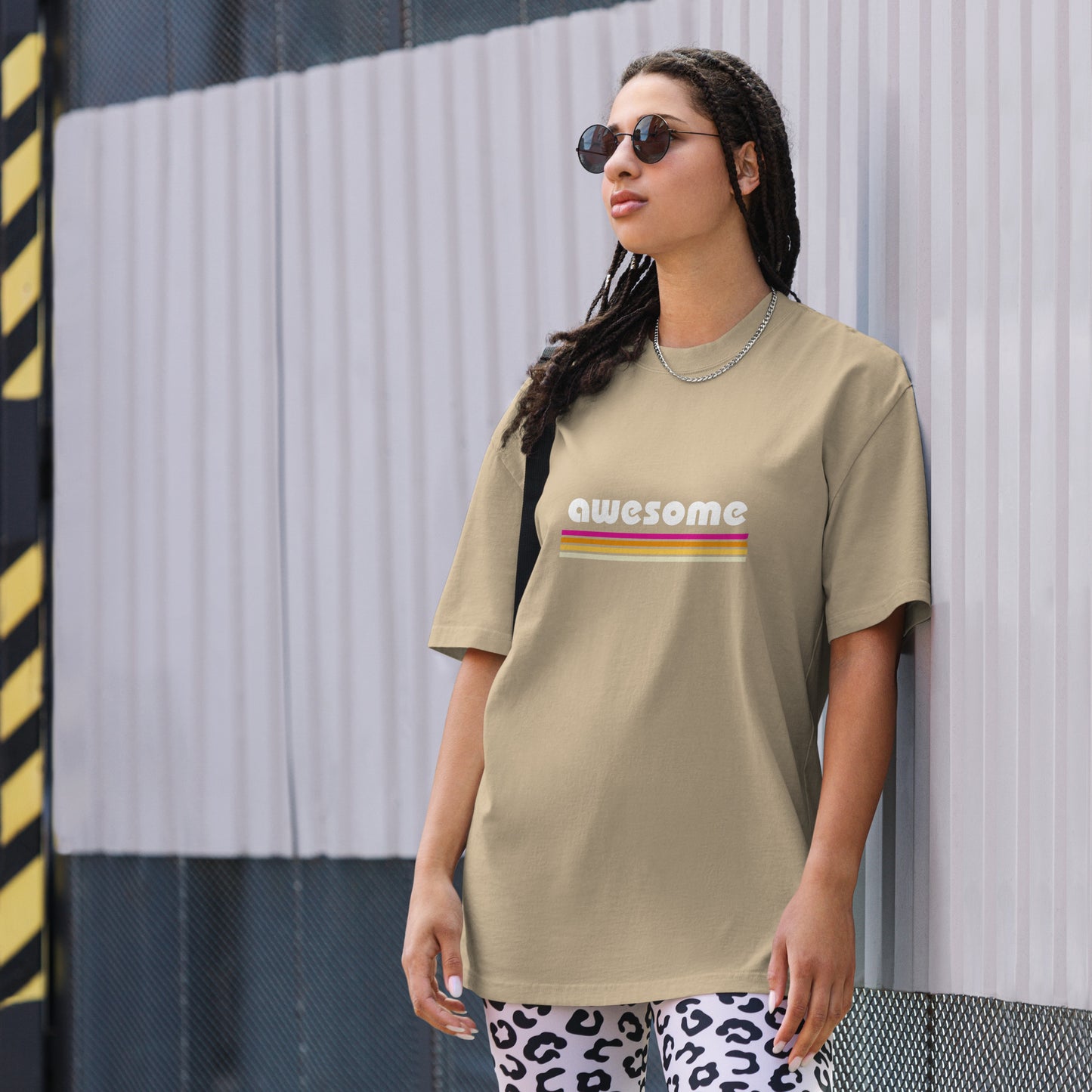 A trendy woman sports a Women's Retro 'AWESOME'  faded eucalyptus Oversized Tee , paired with playful patterned pants and accessorized with sunglasses, reflecting a cool, vintage vibe. Tee available from S-3XL.