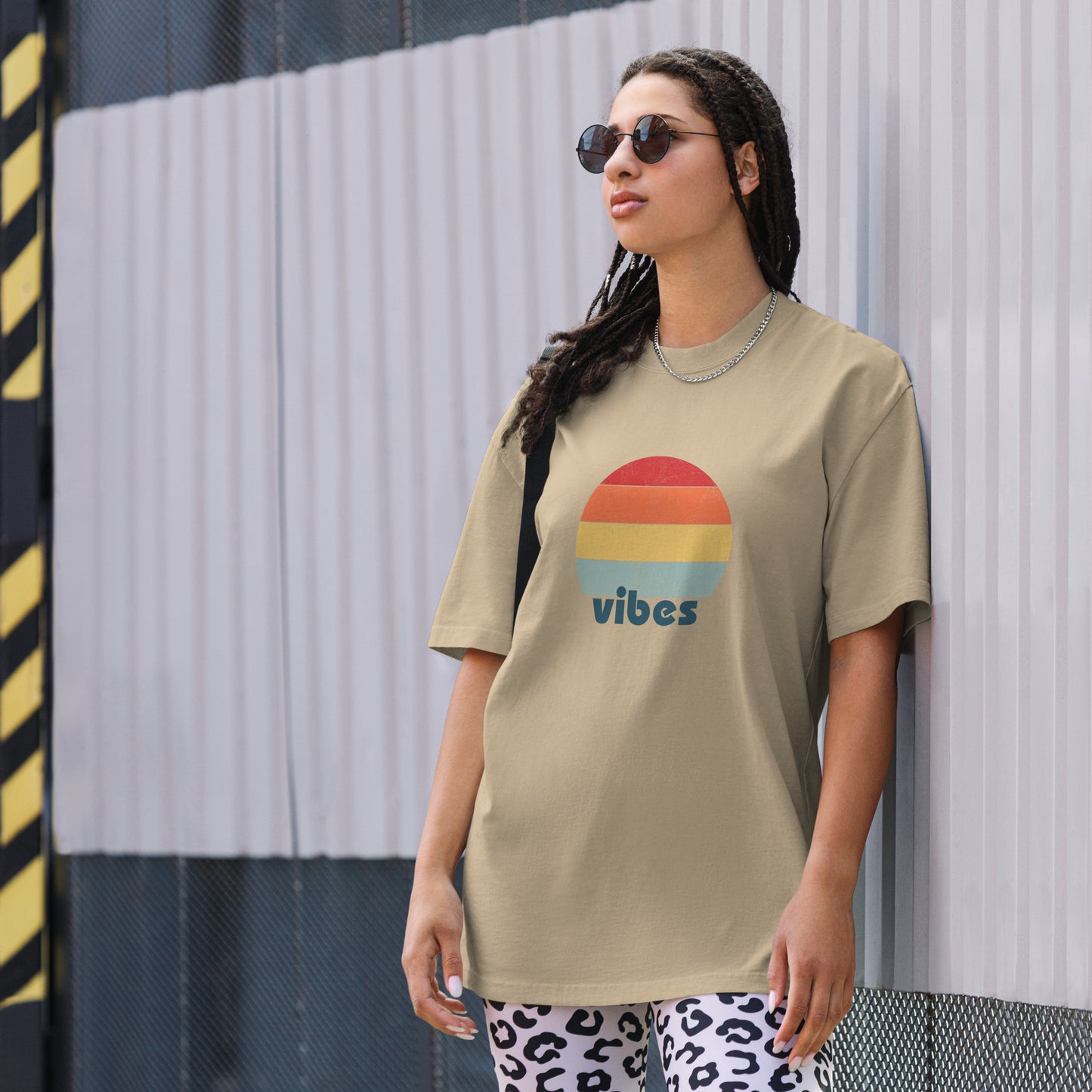 Confident woman showcasing a Women's 'vibes' faded khaki Oversized Tee with a retro-inspired sunset graphic, radiating laid-back, positive vibes in a neutral color, complemented by chic sunglasses. 