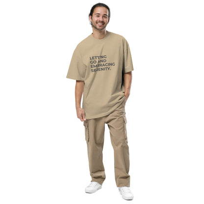 Man wearing a faded khaki oversized faded tee in off-white with "Letting Go and Embracing Serenity" text. 