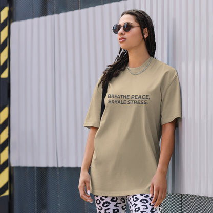 A woman wearing a faded khaki "Breath peace, exhale stress" t-shirt, styled with leopard print leggings and sunglasses, leaning against a corrugated metal wall with a confident expression. The casual yet trendy outfit showcases self-expression and boldness. Perfect for promoting empowering fashion statements.