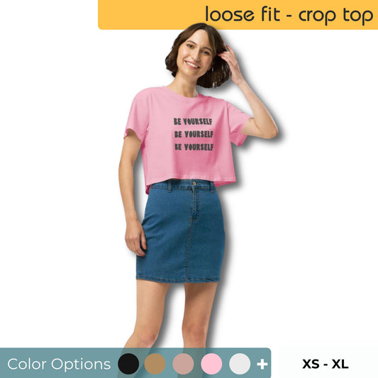 Smiling woman in a pink loose-fit crop top with "Be Yourself" slogan, paired with a blue denim skirt, available in multiple colors, sizes XS to XL.