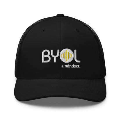 Black retro trucker hat with "BYOL a mindset" embroidered on the front in gray and yellow, displayed against a clean background. Available in various colors: black, white, brown, green, and beige.