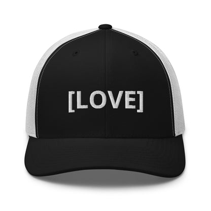 Black and white trucker cap with the word 'LOVE' embroidered in white within brackets, symbolizing an inclusive message, featuring a mesh back and available in multiple colors.