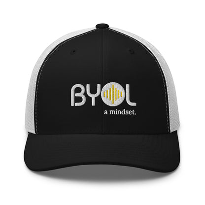 White and black retro trucker hat with "BYOL a mindset" embroidered on the front in gray and yellow, displayed against a clean background. Available in various colors: black, white, brown, green, and beige.