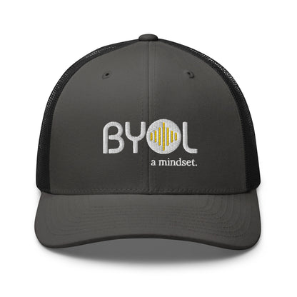 Grey and black retro trucker hat with "BYOL a mindset" embroidered on the front in gray and yellow, displayed against a clean background. Available in various colors: black, white, brown, green, and beige.