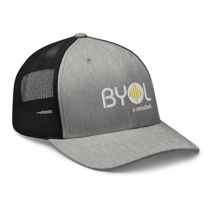 Grey and black retro trucker hat with "BYOL a mindset" embroidered on the front in white and yellow, displayed against a clean background. Available in various colors: black, white, brown, green, and beige.