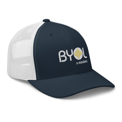 Navy blue and white retro trucker hat with "BYOL a mindset" embroidered on the front in white and yellow, displayed against a clean background. Available in various colors: black, white, brown, green, and beige.