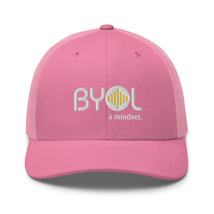 Pink retro trucker hat with "BYOL a mindset" embroidered on the front in gray and yellow, displayed against a clean background. Available in various colors: black, white, brown, green, and beige.