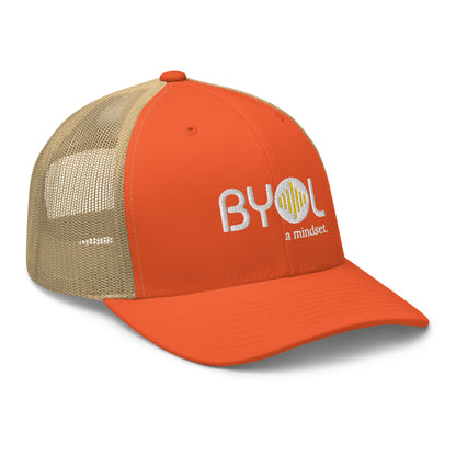 Orange and khaki retro trucker hat with "BYOL a mindset" embroidered on the front in white and yellow, displayed against a clean background. Available in various colors: black, white, brown, green, and beige.