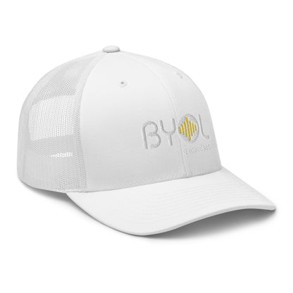 White retro trucker hat with "BYOL a mindset" embroidered on the front in white and yellow, displayed against a clean background. Available in various colors: black, white, brown, green, and beige.