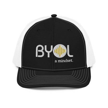 Black and white pre-curved contrast stitched trucker hat with "BYOL a mindset" embroidered on the front in white and yellow, displayed against a clean background. Available in various colors: maroon, black, green, and gray.