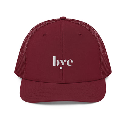 A structured maroon trucker cap mesh back. The front features a white embroidered logo that reads "b.y.e" in lowercase letters. The cap has a curved brim with stitching detail and an adjustable snapback closure at the rear.