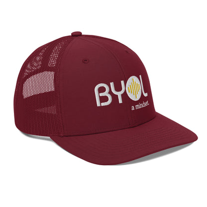 Maroon pre-curved contrast stitched trucker hat with "BYOL a mindset" embroidered on the front in white and yellow displayed against a clean background. Available in various colors: maroon, black, green, and gray.