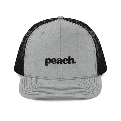 A front view of an grey and black snapback trucker cap, featuring the word "peach." in a casual black script embroidered on the front panel. The cap has a pre-curved visor, a button top, and breathable mesh panels on the sides and back for a comfortable fit.