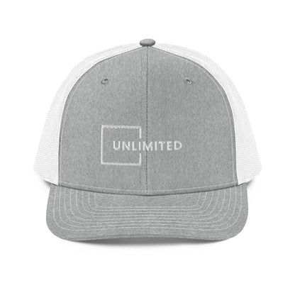 A grey and white snapback trucker cap featuring the word "UNLIMITED" in white block letters enclosed within a white line square, embroidered on the front panel. The cap has a pre-curved visor, structured crown, breathable mesh panels on the sides and back, and an adjustable snap closure for a comfortable fit.