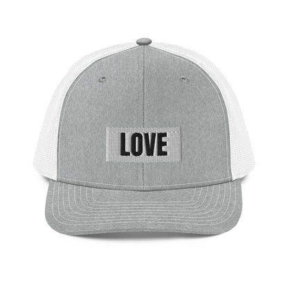 A grey and white snapback trucker cap with the word "LOVE" in white block letters inside a white rectangle, embroidered on the front panel. The hat features a curved brim, white mesh back panels for ventilation, and an adjustable snap closure for a comfortable, custom fit.