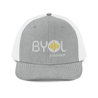 Light grey and white pre-curved contrast stitched trucker hat with "BYOL a mindset" embroidered on the front in white and yellow, displayed against a clean background. Available in various colors: maroon, black, green, and gray.