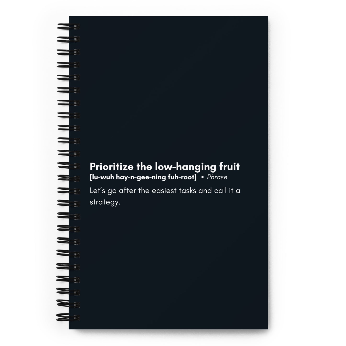 A black spiral-bound notebook with a satirical definition of the corporate phrase "Prioritize the low-hanging fruit" in white text on the cover, featuring a pronunciation guide and an explanation that humorously critiques the concept.