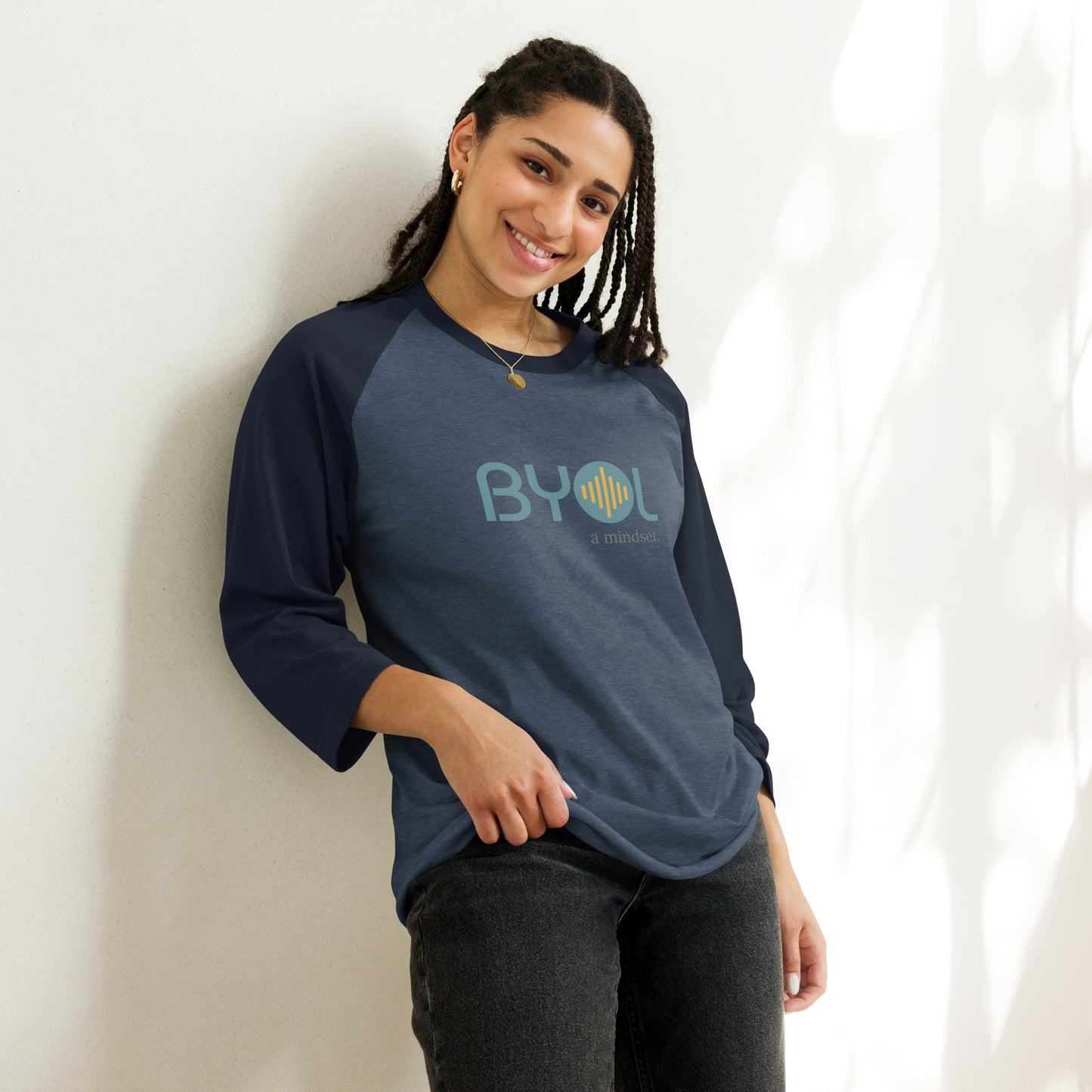 Woman wearing a heather dark blue and navy blue BYOL mindset raglan t-shirt with color options in red, black, gray, and green, available in sizes S to 3XL.