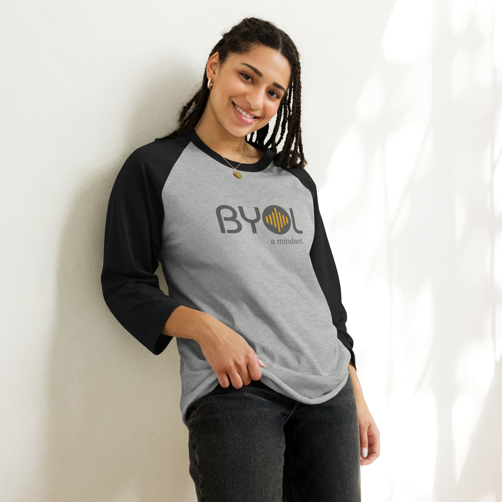 Woman wearing a gray and black BYOL mindset raglan t-shirt with color options in red, black, white, and green, available in sizes S to 3XL.