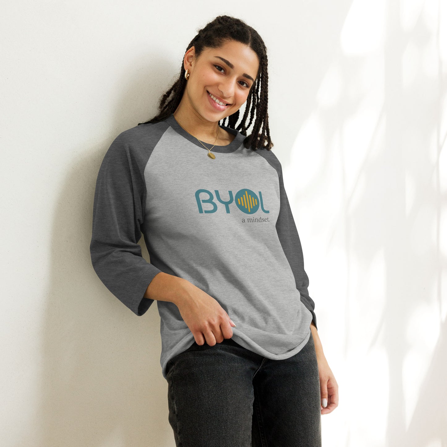 Woman wearing a heather light grey and heather dark grey BYOL mindset raglan t-shirt with color options in red, black, gray, and green, available in sizes S to 3XL.