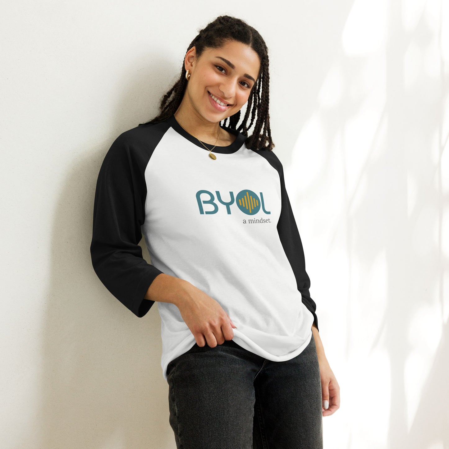 Woman wearing a black and white BYOL mindset raglan t-shirt with color options in red, black, gray, and green, available in sizes S to 3XL.