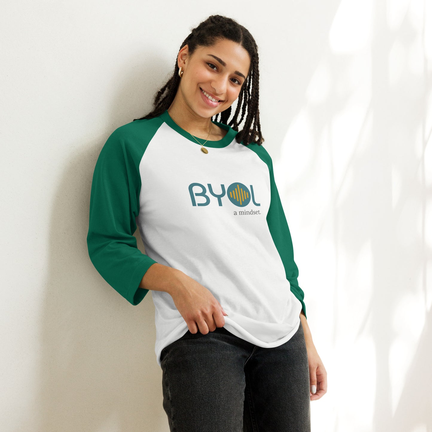 Woman wearing a white and green BYOL mindset raglan t-shirt with color options in red, black, gray, and green, available in sizes S to 3XL.