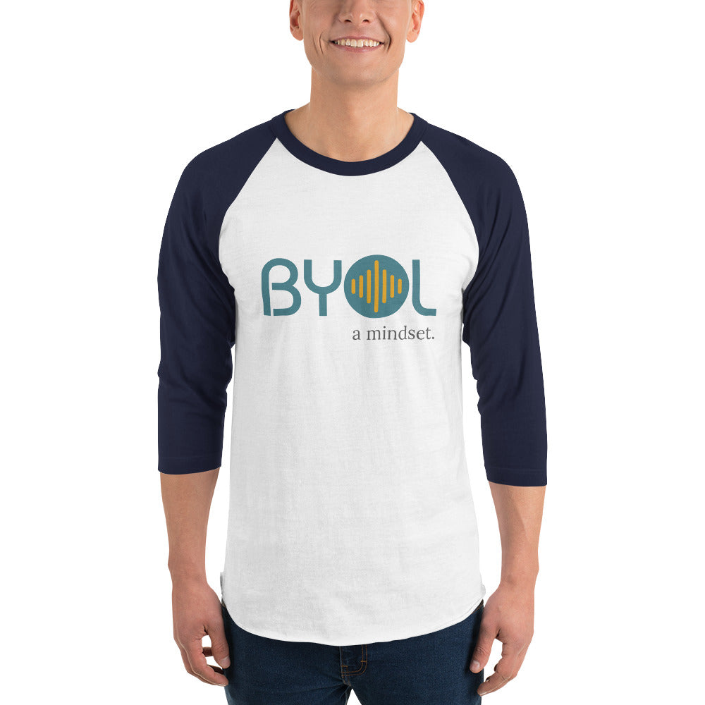 A young man wearing a white and navy blue "BYOL: a mindset" raglan T-shirt with three-quarter sleeves, smiling and standing with his arms at his sides. The T-shirt features the "BYOL" logo in teal and yellow on the front and is available in multiple colors (red, black, white, green, plus more) and sizes (S-3XL). The "be you out loud" logo is displayed at the top.