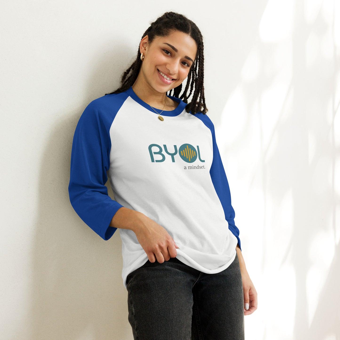 Woman wearing a white and royal blue BYOL mindset raglan t-shirt with color options in red, black, gray, and green, available in sizes S to 3XL.