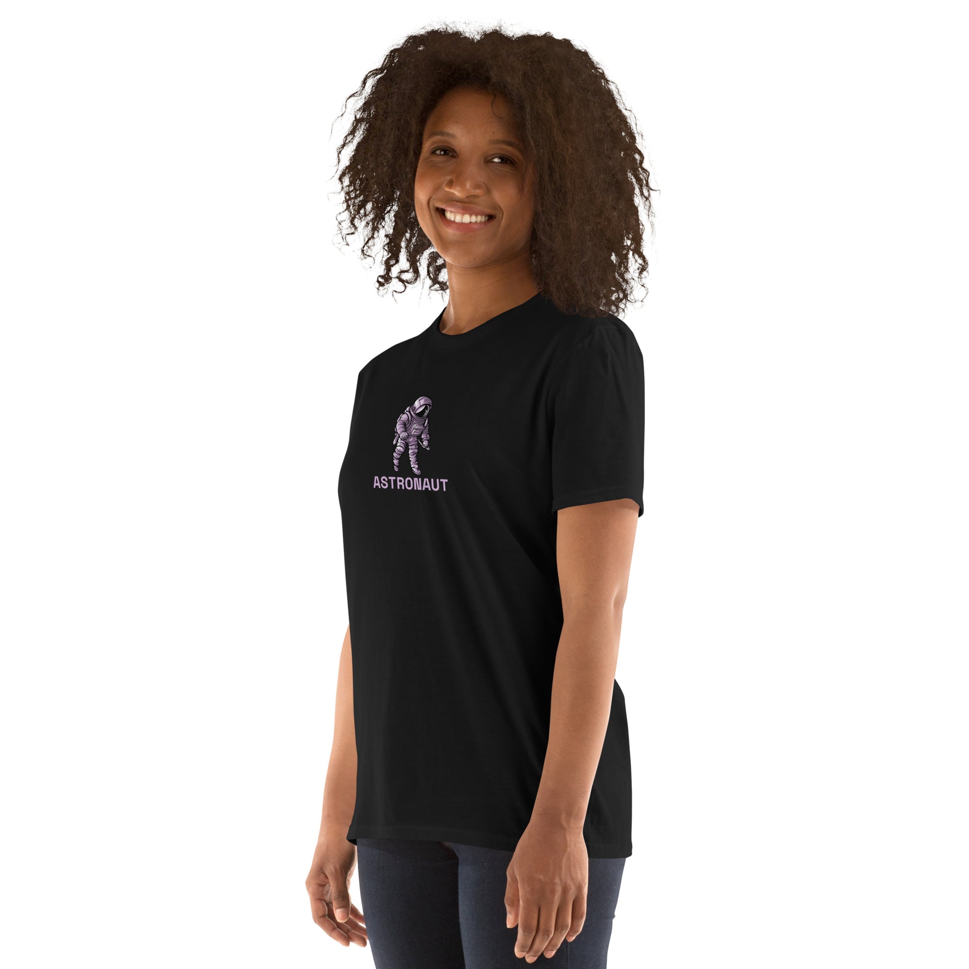 A cheerful woman with curly hair is wearing a black t-shirt featuring a small graphic of an astronaut with the word "ASTRONAUT" beneath it, suggesting a theme of exploration and adventure.