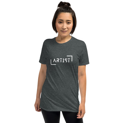 A woman with her hair in a bun is wearing a heathered grey t-shirt that boldly states "ARTIST" in white, bracketed letters, showcasing a strong sense of identity and creative expression.