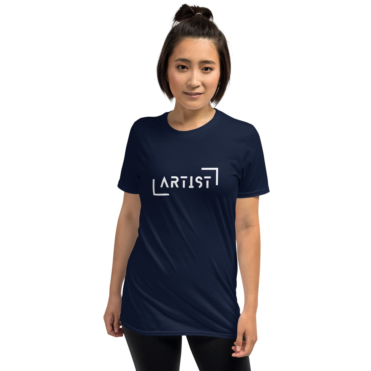 A woman with her hair in a bun is wearing a navy blue t-shirt that boldly states "ARTIST" in white, bracketed letters, showcasing a strong sense of identity and creative expression.