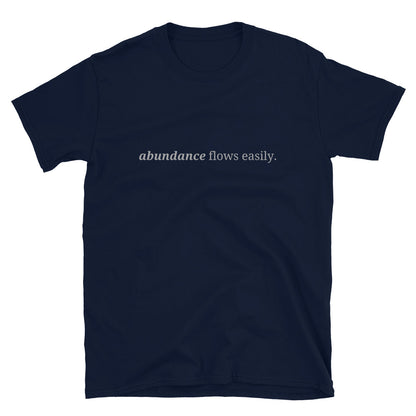 Navy blue t-shirt with the phrase "abundance flows easily." printed on the front, available in color options black, navy blue, gray, white, and light blue, available in sizes S to 3XL.