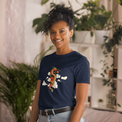 A woman with a confident smile is wearing a navy blue t-shirt with a vibrant, multicolored dragon graphic amongst clouds, symbolizing power and mystique. She's in a cozy, plant-filled space that adds a touch of nature's tranquility to the image.