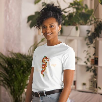 A woman with a confident smile is wearing a white t-shirt with a vibrant, multicolored dragon graphic amongst clouds, symbolizing power and mystique. She's in a cozy, plant-filled space that adds a touch of nature's tranquility to the image.