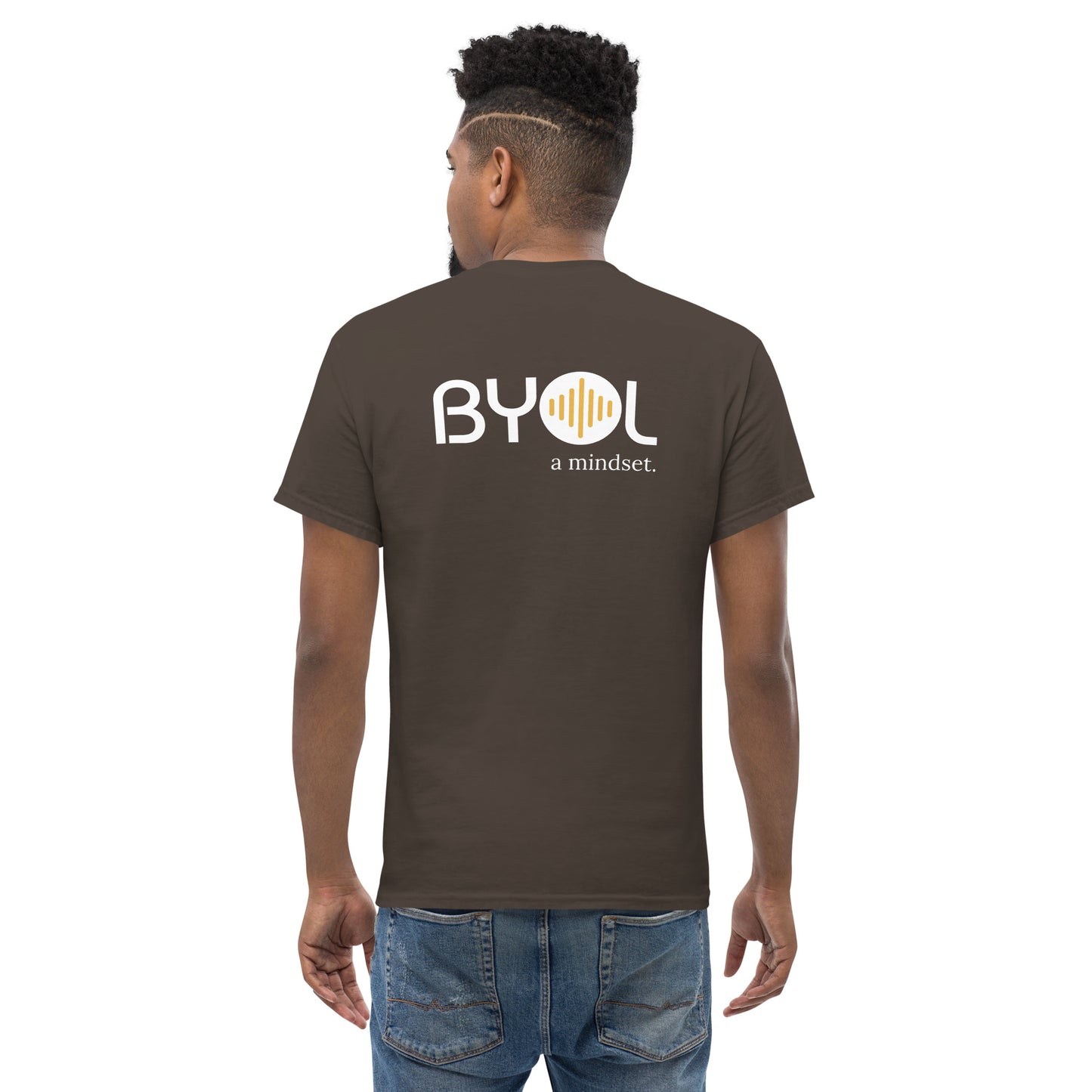 A young man with short curly hair wearing an brown "BYOL: a mindset" T-shirt, viewed from the back. The T-shirt features the "BYOL" logo in white and yellow on the back and is available in multiple colors (maroon, black, brown, gold, plus more) and sizes (S-3XL). The "be you out loud" logo is displayed at the top.