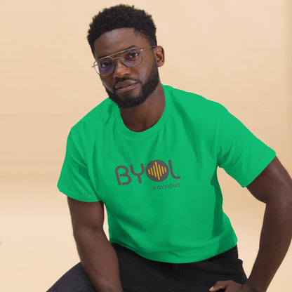 A young man with short curly hair and glasses wearing a green "BYOL: a mindset" T-shirt, sitting down. The T-shirt features the "BYOL" logo in gray and yellow on the front and is available in multiple colors (maroon, black, brown, gold, plus more) and sizes (S-3XL). The "be you out loud" logo is displayed at the top.