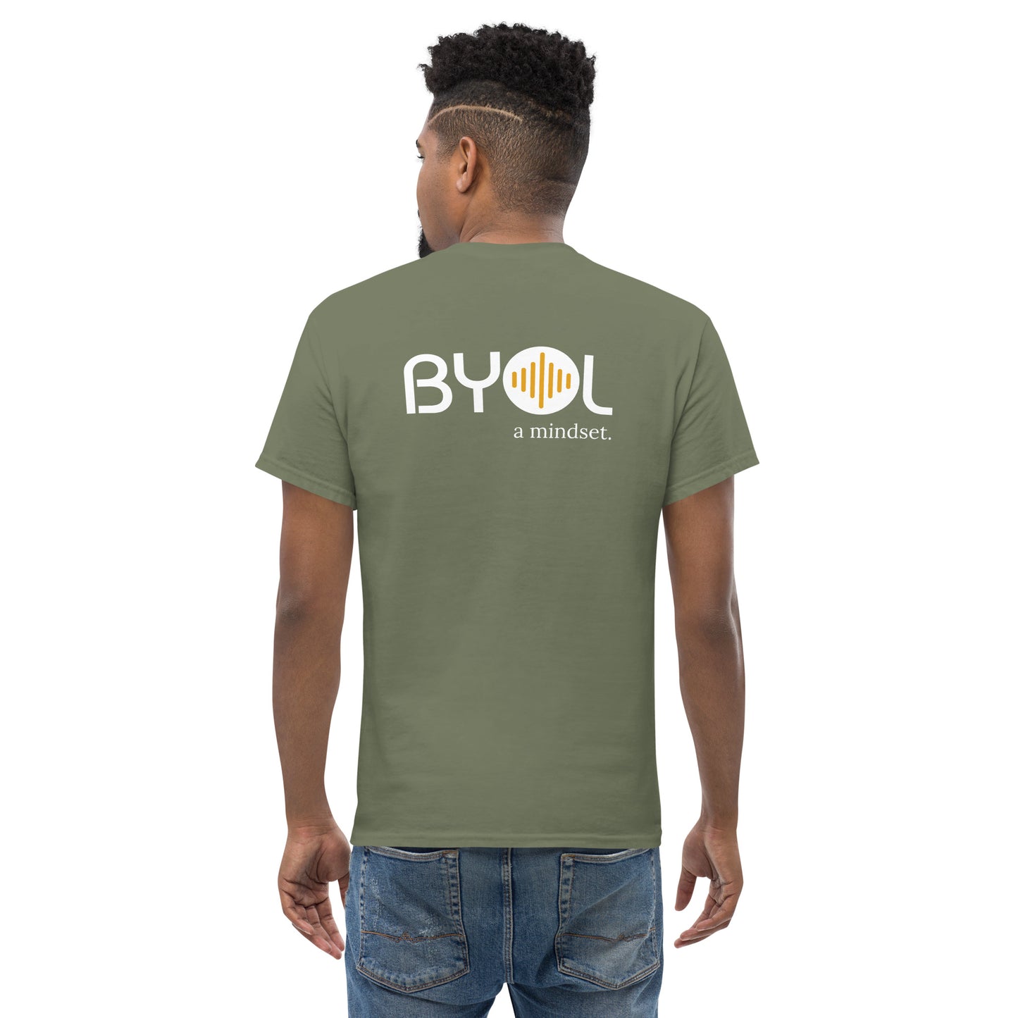 A young man with short curly hair wearing an military green "BYOL: a mindset" T-shirt, viewed from the back. The T-shirt features the "BYOL" logo in white and yellow on the back and is available in multiple colors (maroon, black, brown, gold, plus more) and sizes (S-3XL). The "be you out loud" logo is displayed at the top.