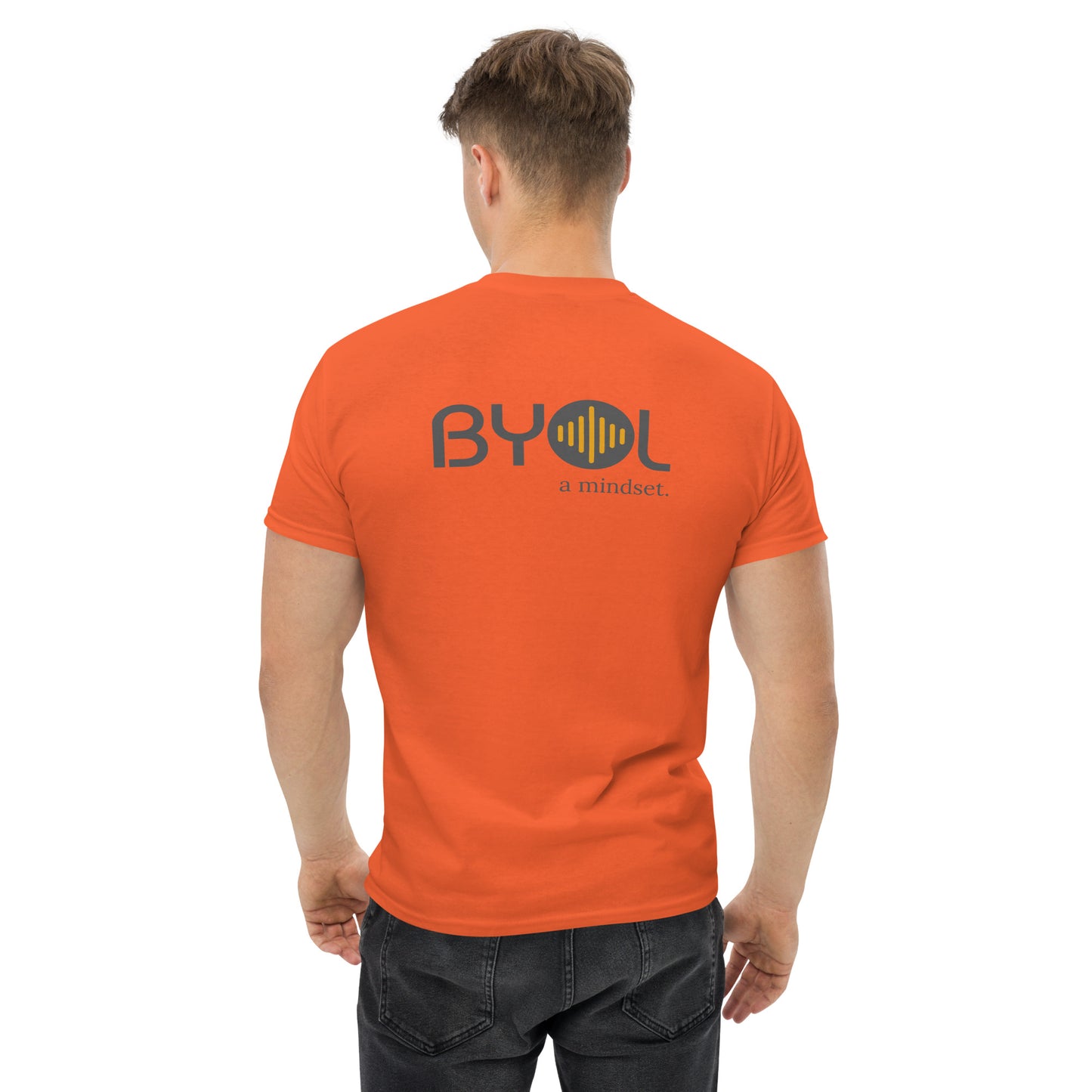 A young man with short blonde hair wearing a orange "BYOL: a mindset" T-shirt, viewed from the back. The T-shirt features the "BYOL" logo in gray and yellow on the back and is available in multiple colors (maroon, black, brown, gold, plus more) and sizes (S-3XL). The "be you out loud" logo is displayed at the top.