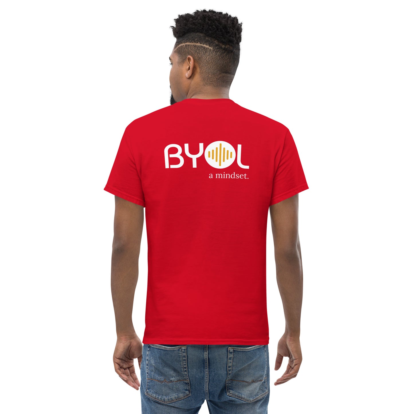 A young man with short curly hair wearing an red "BYOL: a mindset" T-shirt, viewed from the back. The T-shirt features the "BYOL" logo in white and yellow on the back and is available in multiple colors (maroon, black, brown, gold, plus more) and sizes (S-3XL). The "be you out loud" logo is displayed at the top.