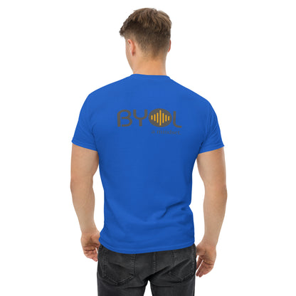 A young man with short blonde hair wearing a royal blue "BYOL: a mindset" T-shirt, viewed from the back. The T-shirt features the "BYOL" logo in gray and yellow on the back and is available in multiple colors (maroon, black, brown, gold, plus more) and sizes (S-3XL). The "be you out loud" logo is displayed at the top.