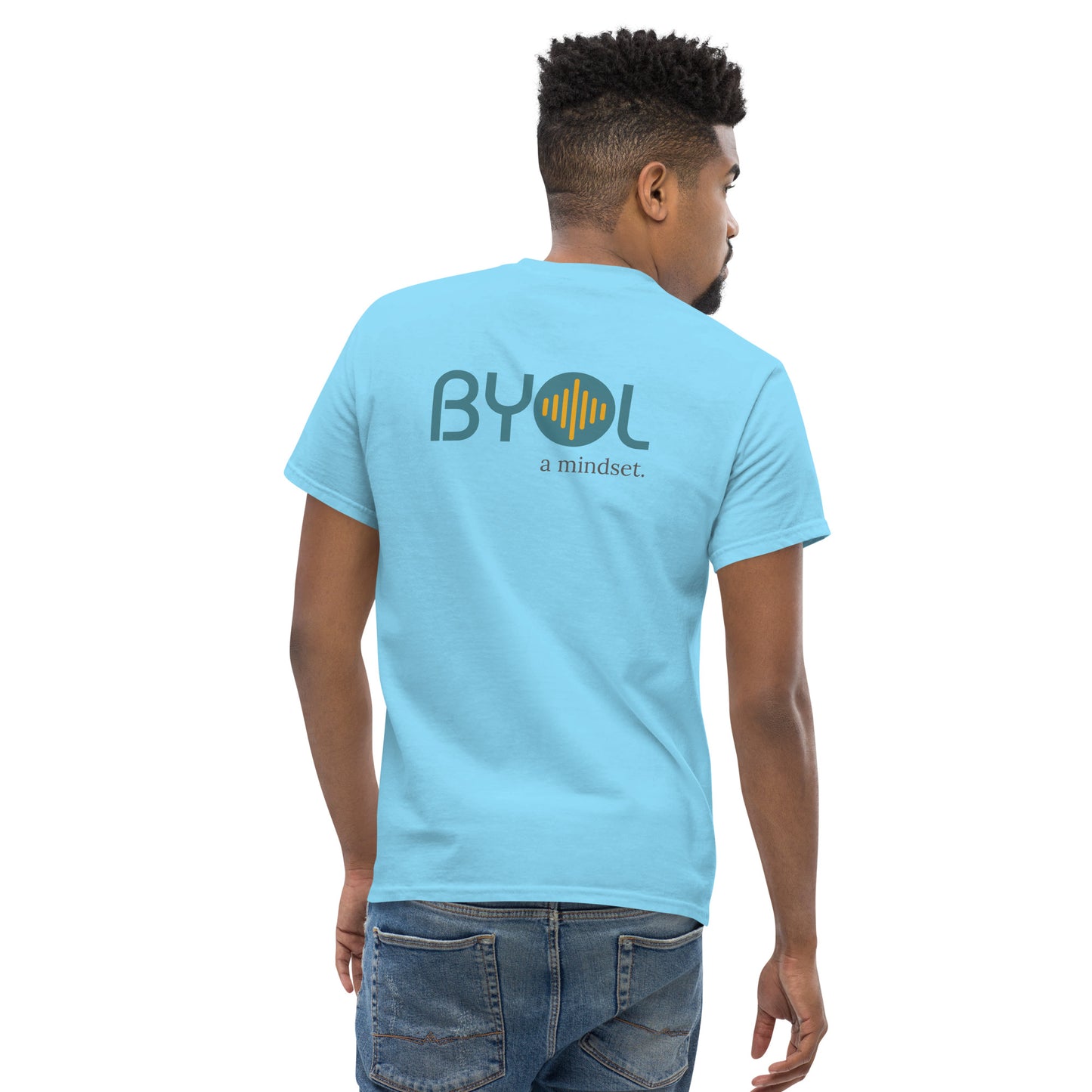 A young man with short hair wearing a sky "BYOL: a mindset" T-shirt, viewed from the back. The T-shirt features the "BYOL" logo in teal and yellow on the back and is available in multiple colors (maroon, black, brown, gold, plus more) and sizes (S-3XL). The "be you out loud" logo is displayed at the top.