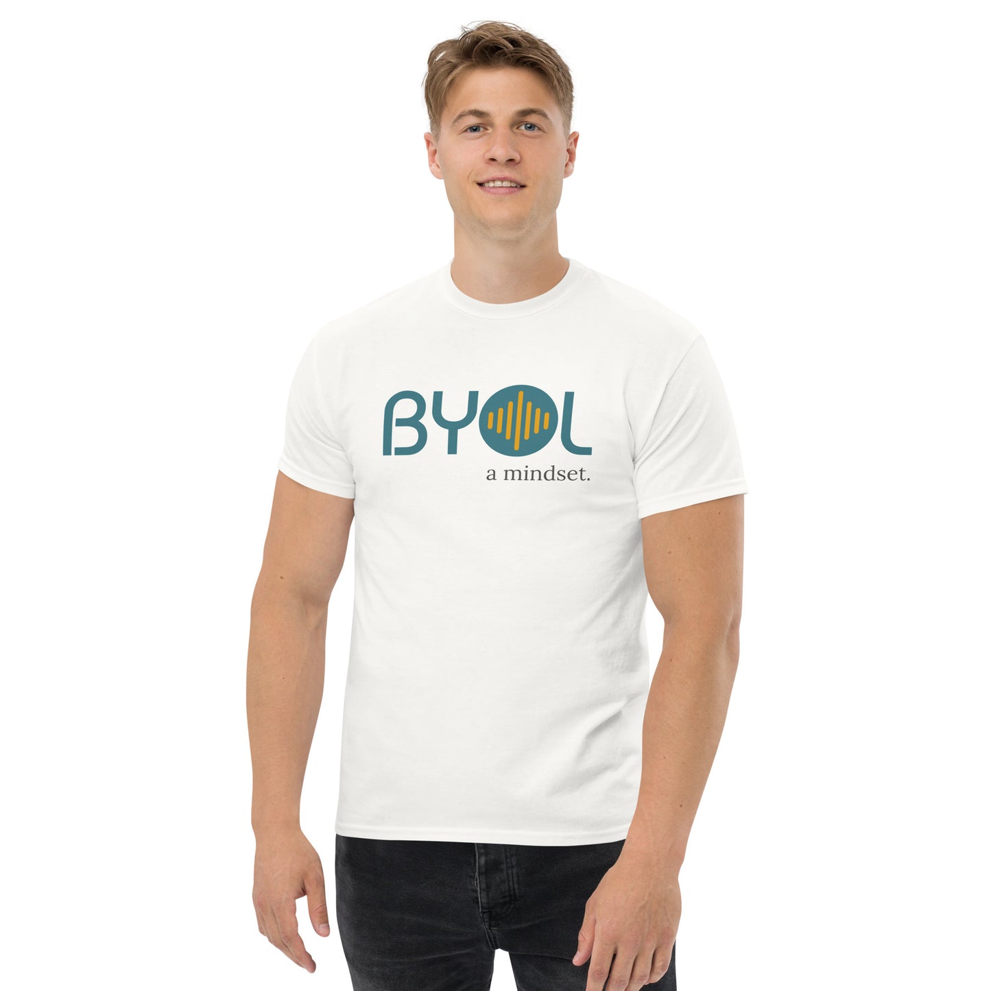 A young man with short blonde hair wearing a white "BYOL: a mindset" T-shirt, smiling and standing with his arms at his sides. The T-shirt features the "BYOL" logo in teal and yellow on the front and is available in multiple colors (maroon, black, brown, gold, plus more) and sizes (S-3XL). The "be you out loud" logo is displayed at the top.