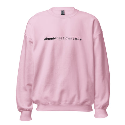 Pink sweatshirt with the phrase "abundance flows easily." printed on the front, available in color options navy blue, green, maroon, gray, and pink, available in sizes S to 3XL.