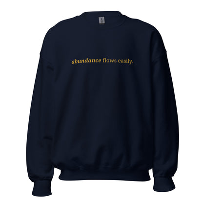 Navy blue sweatshirt with the phrase "abundance flows easily." printed on the front, available in color options navy blue, green, maroon, gray, and pink, available in sizes S to 3XL.