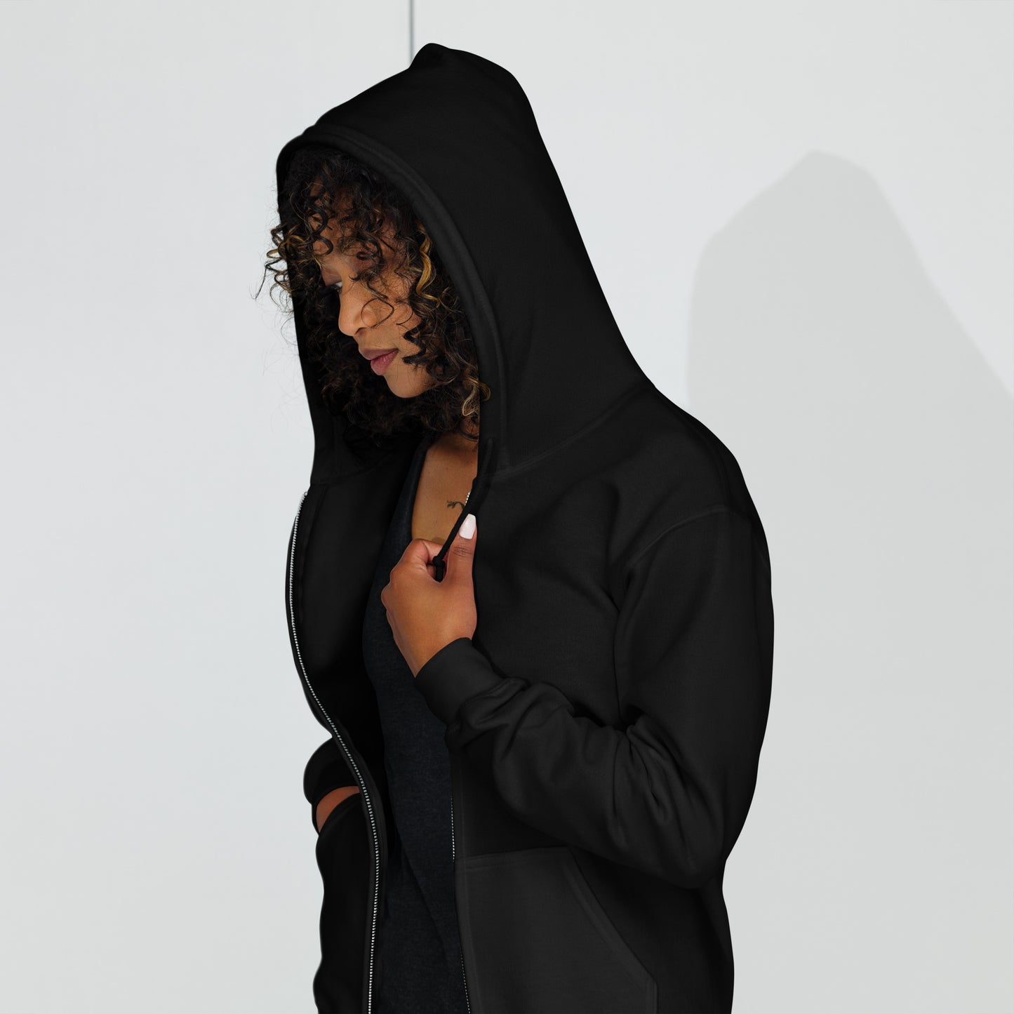 Woman wearing a black BYOL mindset zip-up hoodie with hood up and hands in pockets, available in various sizes.