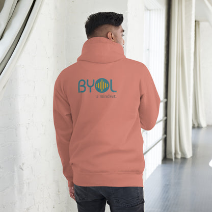 A young man wearing a dusty rose "BYOL: a mindset" hoodie, viewed from the back. The hoodie features the "BYOL" logo in teal and yellow on the back and is available in multiple colors (black, red, maroon, brown, plus more) and sizes (S-3XL). The "be you out loud" logo is displayed at the top.